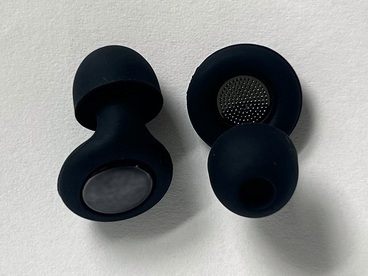Two Quiet earplugs side by side: one turned to show the fine perforated acoustic mesh filter set into its inner face, one showing its soft silicone tip