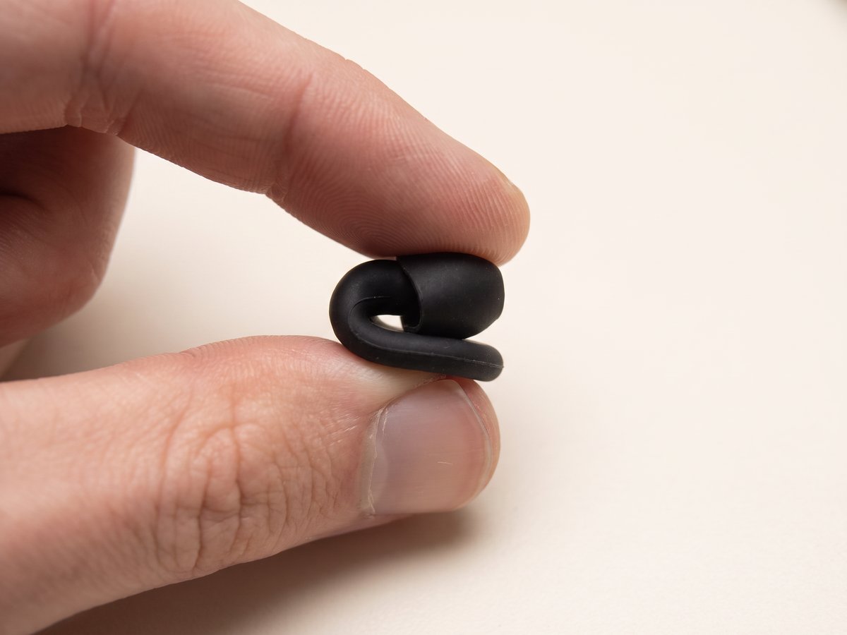 A Quiet earplug pinched between finger and thumb and folded almost in half, showing how soft the silicone is