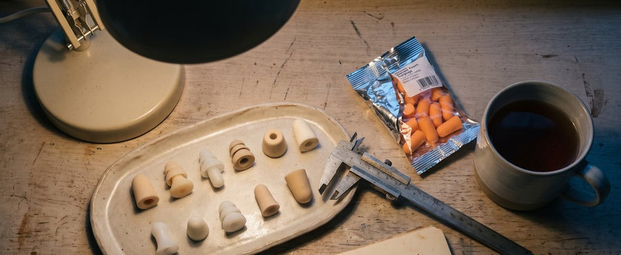 A workbench of earplug prototypes, calipers and a torn-open pack of generic foam plugs